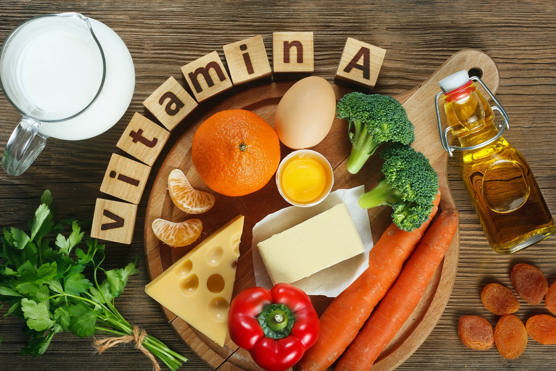 Visão superior de tábua de madeira redonda contendo alimentos ricos em vitamina A e o texto Vitamin A escrito com letras em  blocos de madeira no contorno superior da tábua