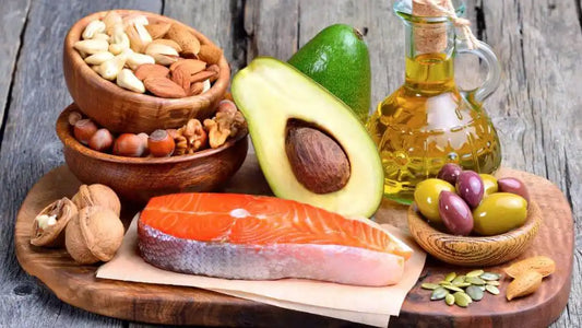 Tábua de madeira contendo azeite ,nozes, abacate, azeitnoas e azeite sobre mesa de madeira