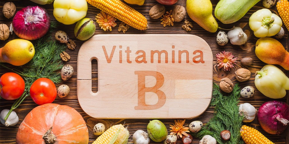 Tábua de madeira retangular com cantos arredondados com o texto Vitamina B escrito e rodeada de vegetais rico em vitamina B